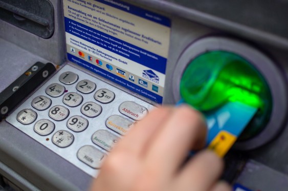 a close-up photo of a person punching in their PIN on an ATM in a wall.
