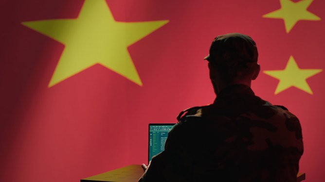 A man sits in front of a computer and the Chinese flag.