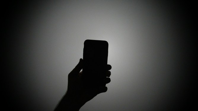 The silhouette of a hand holding an iPhone with the light on.