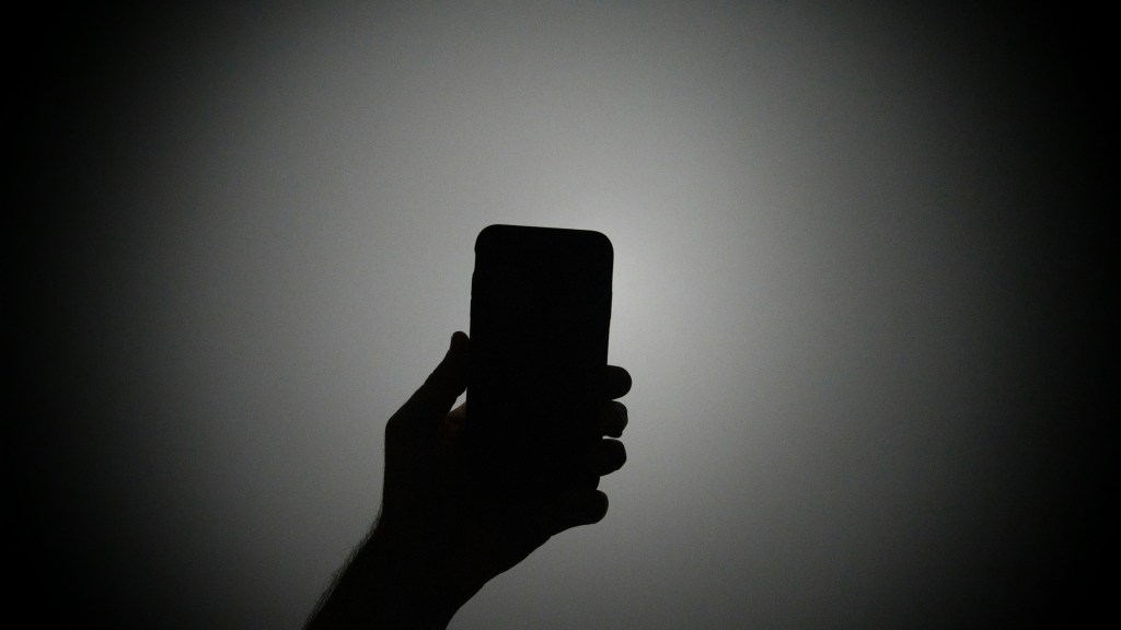 The silhouette of a hand holding an iPhone with the light on.