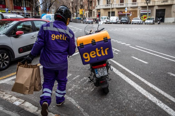 Getir delivery driver holding grocery bags and walking to Getir delivery bike.