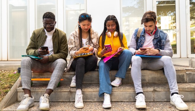 Group of multiracial teenage college friend students ignoring each other looking at mobile phone.