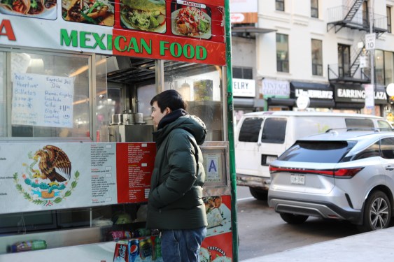A man places an order at a Mexican food cart.