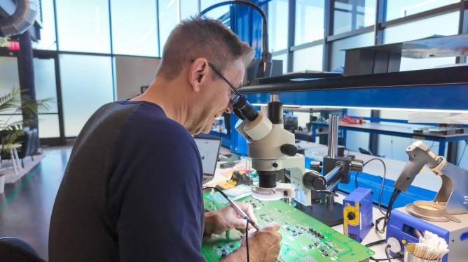 man looking circuit board thru microscope